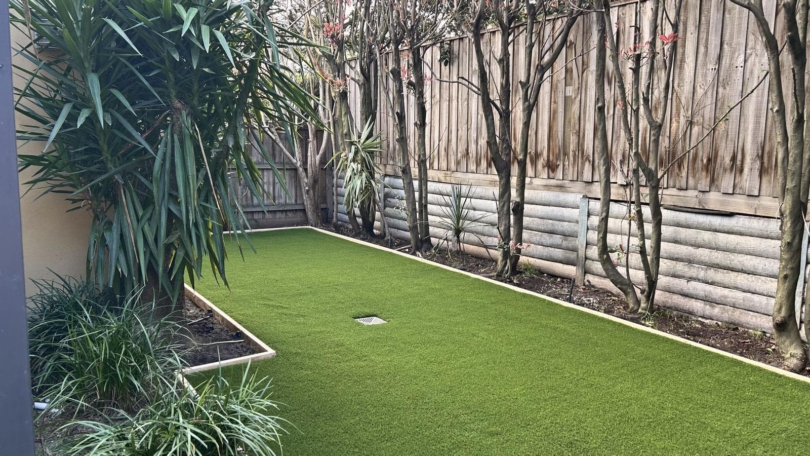 Finished back garden with synthetic lawn and timber edging along a paling fence, Burwood