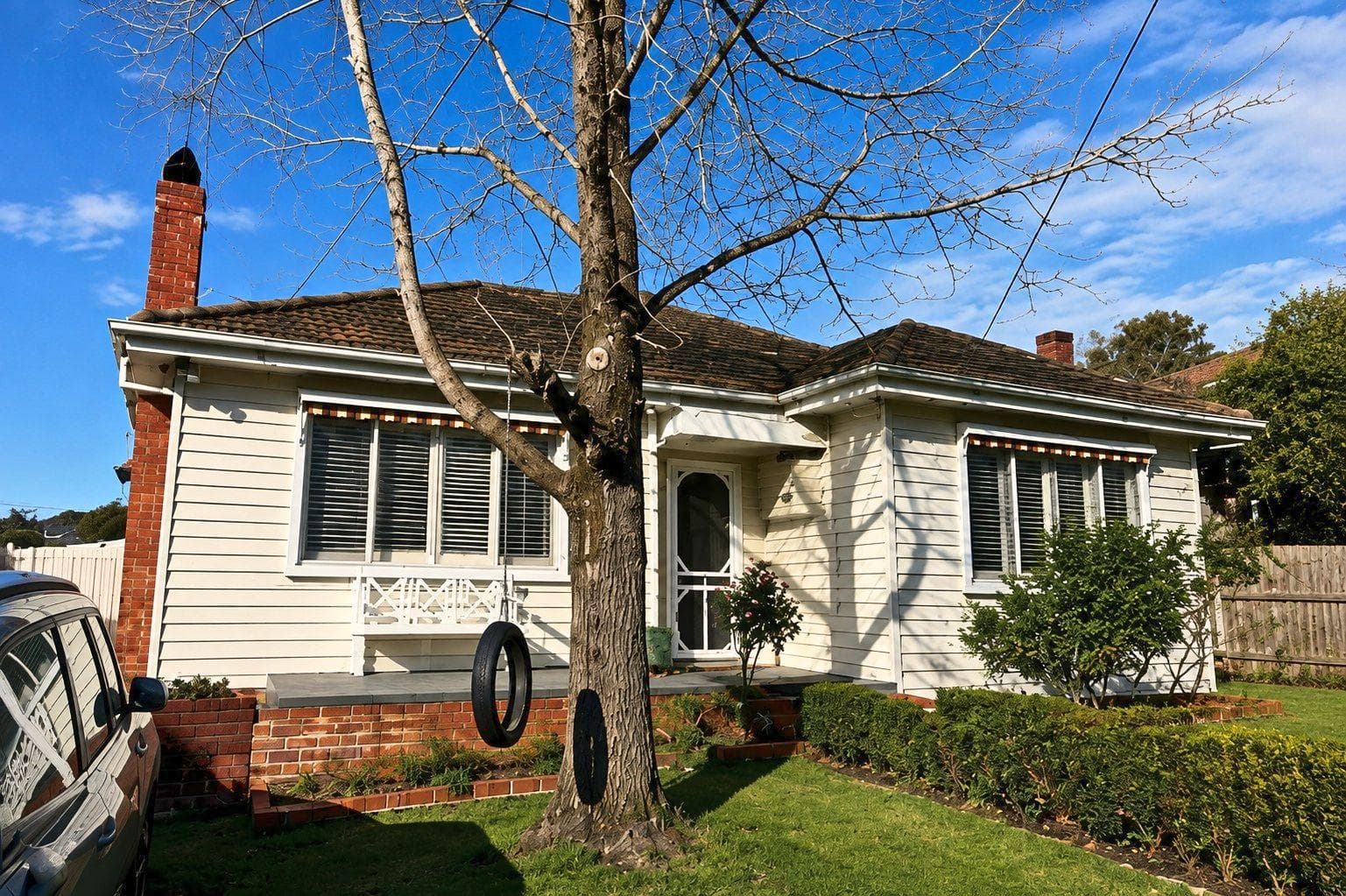 Bare deciduous tree in the front lawn of a weatherboard house, Burwood