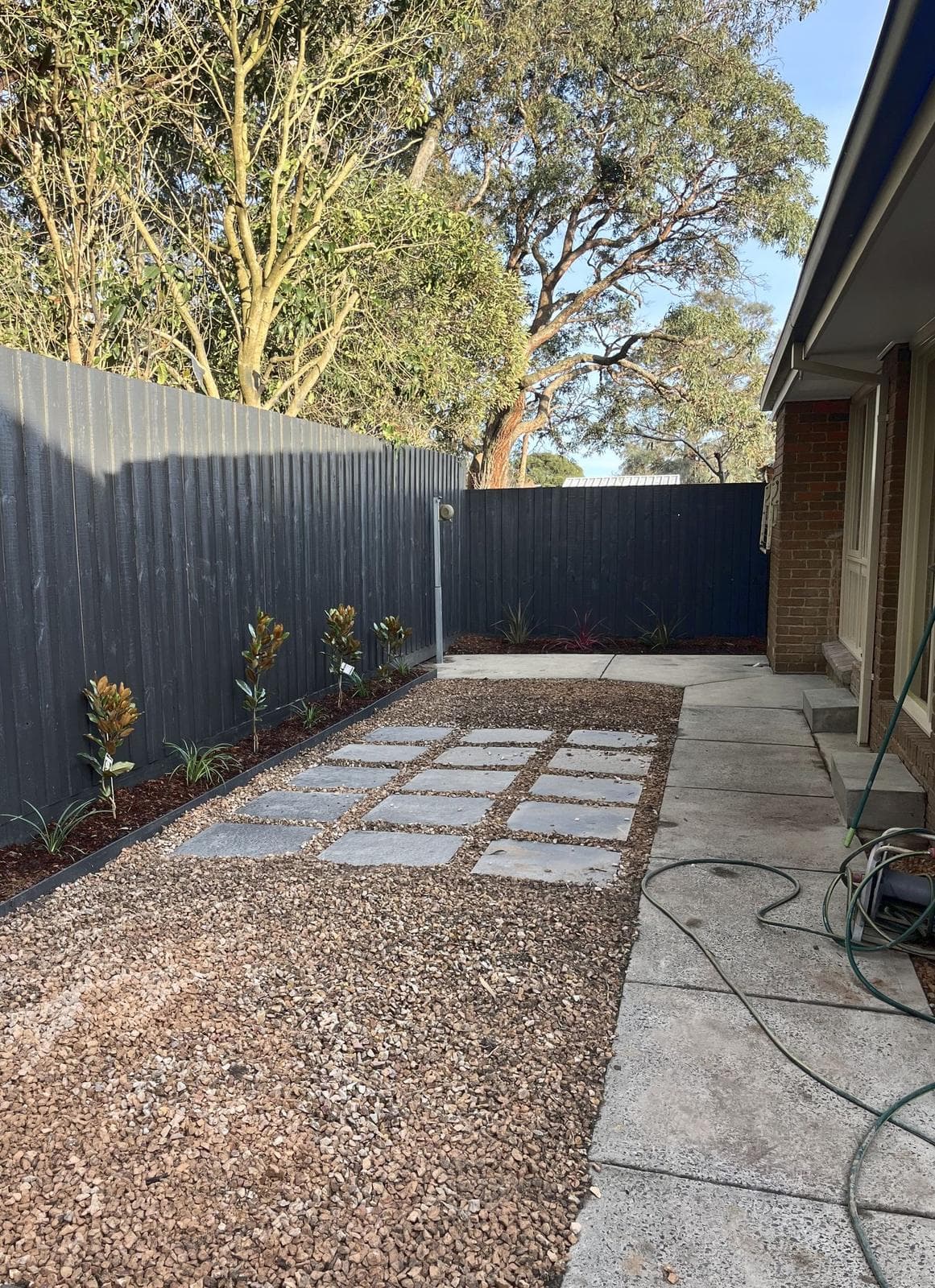 Same side yard finished with gravel, square pavers and magnolias along a charcoal fence, Forest Hill